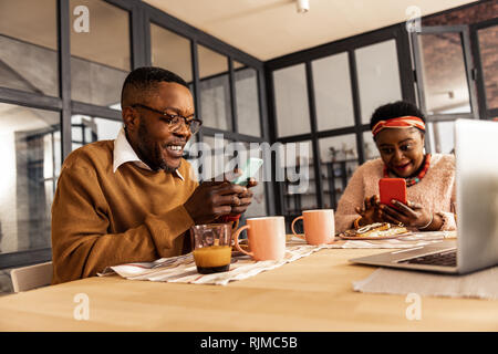 Delighted joyful couple being engaged in their smartphones Stock Photo