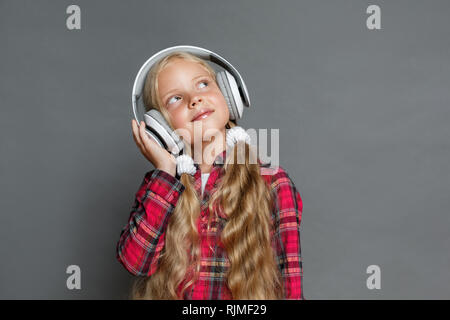 Little girl in headphones with ponytails standing isolated on grey ...