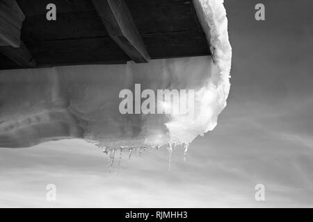 Black and white wooden roof with hang down snow cornice and icicle at sun winter day Stock Photo