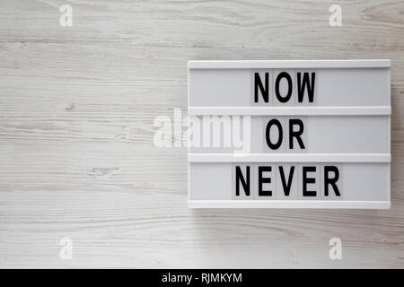 Modern board with text 'Now or never' word on modern board on a white wooden surface, top view. Copy space. Stock Photo