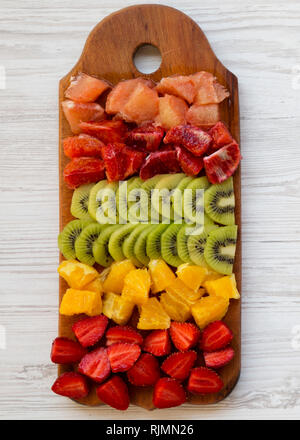Chopped fresh fruits arranged on cutting board on white wooden surface. Flat lay, overhead. Stock Photo