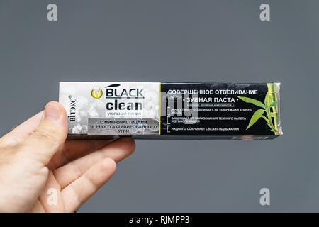 PARIS, FRANCE - JUL 28, 2018: Man holding ukrainian cardboard box of made Vitek's black clean toothpaste made from charcoal against gray background Stock Photo