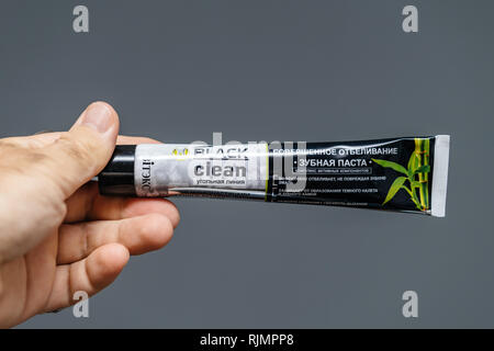 PARIS, FRANCE - JUL 28, 2018: Man holding tube of ukrainian made Vitek's black clean toothpaste made from charcoal against gray background Stock Photo