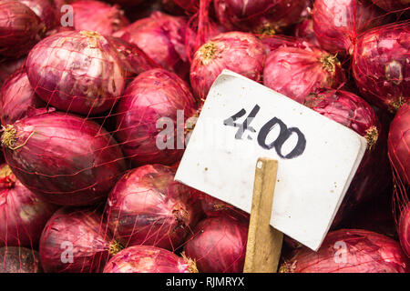 Red onions fresh and organic on sale at a vegetable stand in a food local market with the white price tag on wood stick. Stock Photo