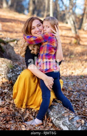 Happy mother and serious daughter hugging each other in the autumn nature background Stock Photo