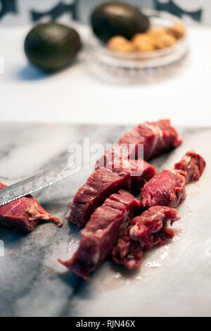 A marbled beef roast on a marble cutting board being cut up with a serrated knife. Stock Photo