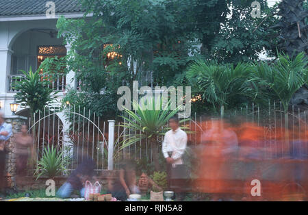 Caption: Luang Prabang, Laos - Sep 2002. Locals giving alms to monks during the ritual morning collection outside the Villa Santi Hotel, an old Royal  Stock Photo