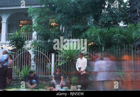 Caption: Luang Prabang, Laos - Sep 2002. Locals giving alms to monks during the ritual morning collection outside the Villa Santi Hotel, an old Royal  Stock Photo