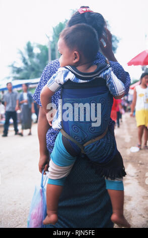 Caption: Luang Prabang, Laos - Sep 2002. A Hmong woman carries her child stapped to her back at the annual boat racing festival in Luang Prabang.  The Stock Photo