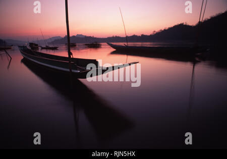 Caption: Luang Prabang, Laos - Jan 2001. The sun setting over the Mekong in the World Heritage town of Luang Prabang in northern Laos.  The long boats Stock Photo