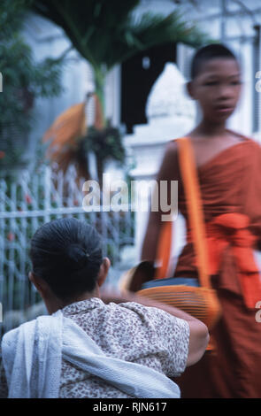 Caption: Luang Prabang, Laos - Sep 2003. A lady is giving alms to a novice monk in the early hours of the morning, Luang Prabang. Supported by the com Stock Photo