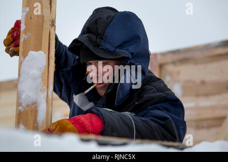 Portrait of a worker in a blue jacket with a hood on his head and a cigarette in his mouth Stock Photo