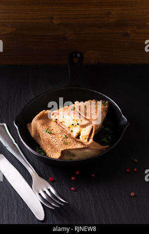 Food concept homemade Ham and Cheese Crepe in iron skillet cast on black slate background Stock Photo