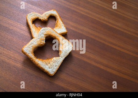 Toasted white bread toasts with heart shape on brown wooden background, love, valentines day Stock Photo