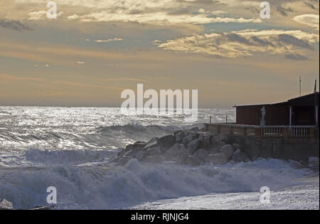 Rough sea in winter in Porto Recanati in the province of Ancona Italy near Monte Conero with the sea crashing on rocks and a boarded up restaurant Stock Photo