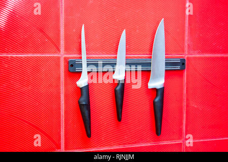 set of high quality kitchen cook knives tools on a magnet board hanging on the red wall Stock Photo