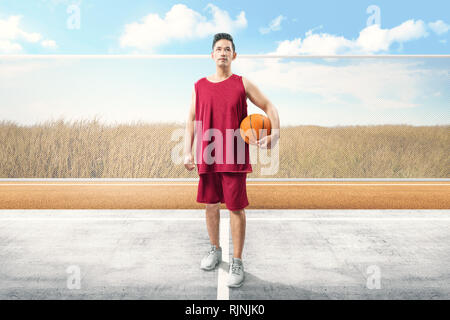 Handsome asian man with sport uniform carrying the ball on the outdoor basketball court Stock Photo