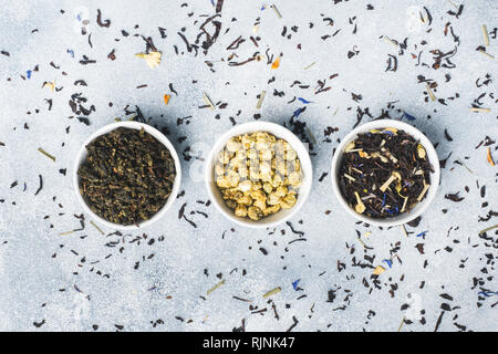 Variety of dry tea leaves and flowers in bowl on grey background Stock Photo