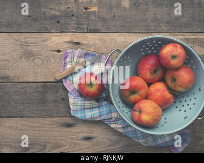 Delicious organic apples in an old used colander on a rustic wooden table, flat tone vintage style with view from above Stock Photo