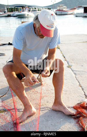 Prvic island, Croatia - August 23, 2018: Fisherman repairing his fishing net on pier with boats in the background Stock Photo