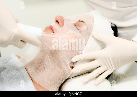 Beautician in white gloves treats  female customer with electric darsonval facial massage, procedure at beauty salon Stock Photo