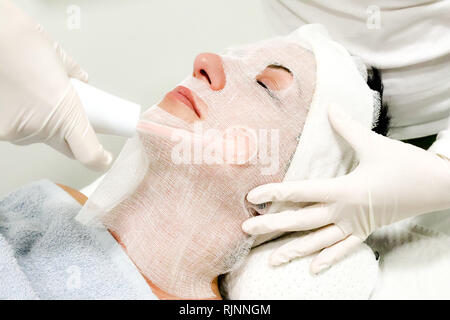 Beautician in white gloves treats  female customer with electric darsonval facial massage, procedure at beauty salon Stock Photo