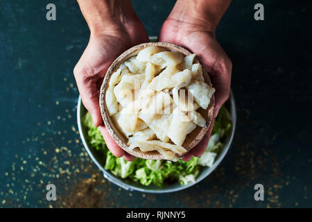 high angle view of a young caucasian man about to prepare xato, a catalan salad with desalinated salt cod and escarole endive, on a rustic dark green  Stock Photo