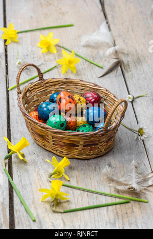 Colorful quail eggs for Easter, in a wicker basket and daffodils. Stock Photo