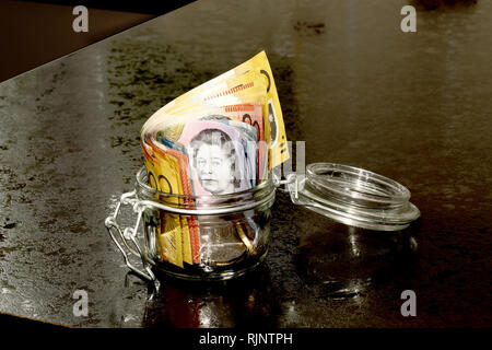 Australian Dollars in a glass jar on a kitchen counter Stock Photo