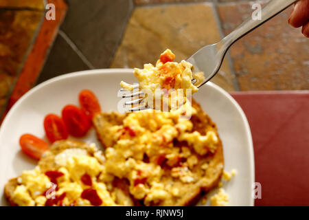 Scrambled egg on toast with plum tomatoes and tomato sauce. Background is a tiled table top. Stock Photo