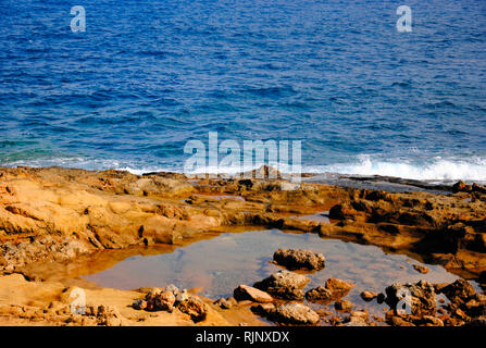 breaking waves at the red rocky coast of Sissi on Crete in Greece Stock Photo