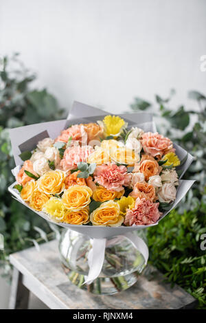beautiful fresh cut bouquet of mixed flowers in vase on wooden table. The work of the florist at a flower shop. Delicate Pastel tones color Stock Photo