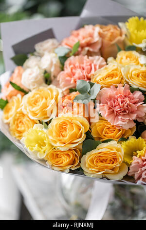 beautiful fresh cut bouquet of mixed flowers in vase on wooden table. The work of the florist at a flower shop. Delicate Pastel tones color Stock Photo