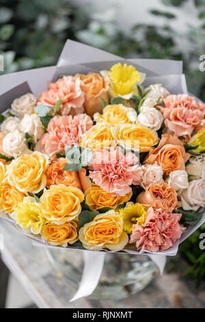 beautiful fresh cut bouquet of mixed flowers in vase on wooden table. The work of the florist at a flower shop. Delicate Pastel tones color Stock Photo