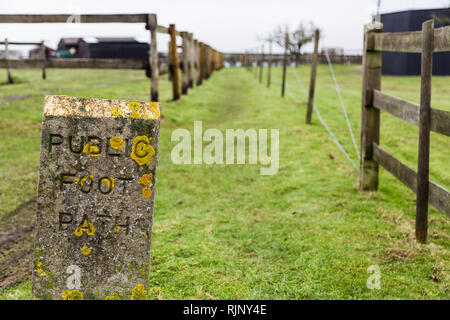 Public footpath stone sign looking weather beaten and covered in moss on an overcast day. The sign is showing access to a pathway in the countryside.