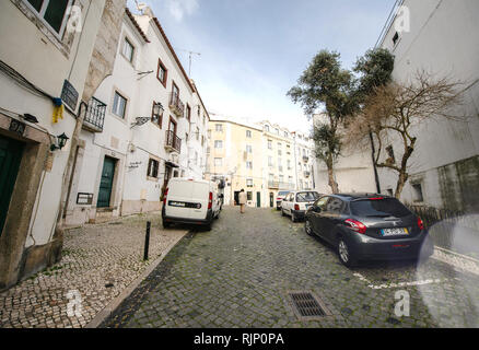 LISBON, PORTUGAL - FEB 10, 2018: Perspective view of cobblestone sidewalk and road with cars and traditional buildings and senior woman walking Stock Photo