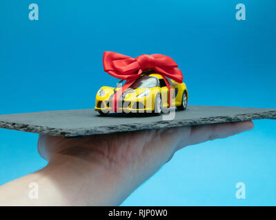 mans hand with small toy car with red bow on black rock plate as a daily dish Stock Photo