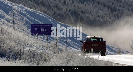 Red car on the A82 road entering the district of Stirling on a sunny day in winter, near Tyndrum, Scotland Stock Photo
