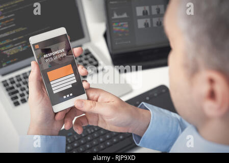 Web designer, programmer working with responsive web template. Multiple devices on desk. Stock Photo