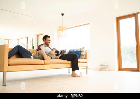 Boy and father using digital tablets whilst reclining on sofa Stock Photo