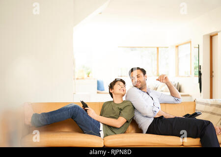 Boy and father using digital tablets back to back on sofa Stock Photo