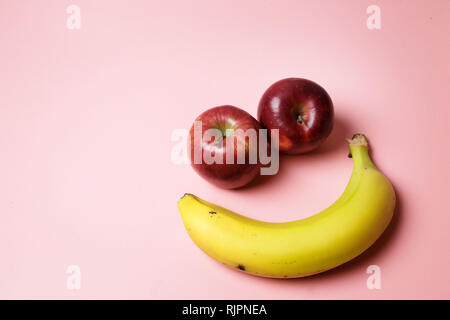 Smiley face with two apples and a banana with copy space on a pink background Stock Photo