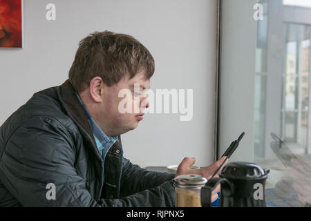 Man with down syndrome using phone by cafe window Stock Photo