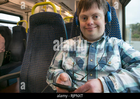 Man with down syndrome with using headphones and cell phone on train Stock Photo