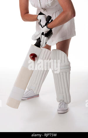 Woman cricketer in a white dress with a safety helmet, shin pads, a bat and ball. Stock Photo