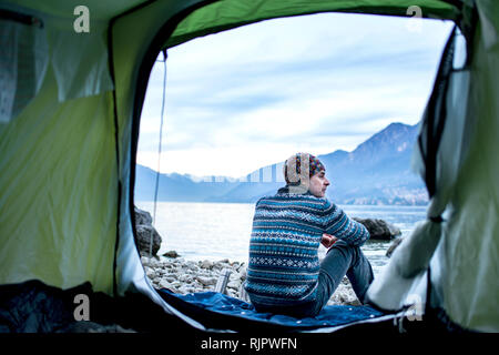 Man camping on lakeside, view from inside tent, Onno, Lombardy, Italy Stock Photo