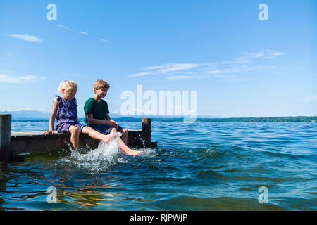 Siblings cooling feet in water, Lake Starnberg, Bavaria, Germany Stock Photo