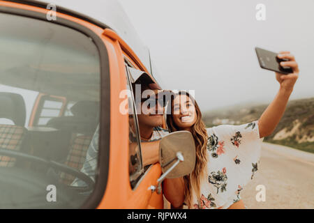 Young couple on roadside in recreational vehicle taking smartphone selfie,  portrait, Jalama, California, USA Stock Photo