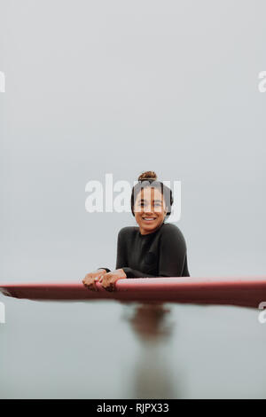 Young female surfer leaning on surfboard in calm misty sea, portrait, Ventura, California, USA Stock Photo