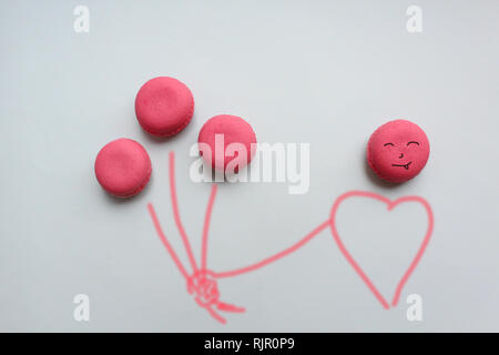 Three pink macaroons in the form of balloons in the hand of man on a blue background. Stock Photo
